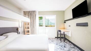 Habitación de hotel con cama, escritorio, silla, televisor montado en la pared y ventana con vistas a zonas verdes.