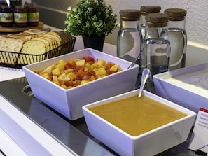 Un buffet avec des saladiers remplis de fruits, un grand récipient de soupe et des pots de condiments.