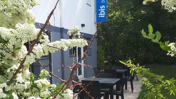 Un espace extérieur aménagé avec des tables et des chaises, entouré d’arbres en fleurs et d’un bâtiment orné d’une enseigne bleue.