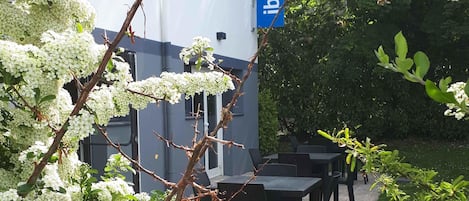 Un espace extérieur aménagé avec des tables et des chaises, entouré d’arbres en fleurs et d’un bâtiment orné d’une enseigne bleue.