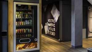 A modern interior with a vending machine stocked with beverages and snacks, a wall with a motivational quote, and a wooden floor.