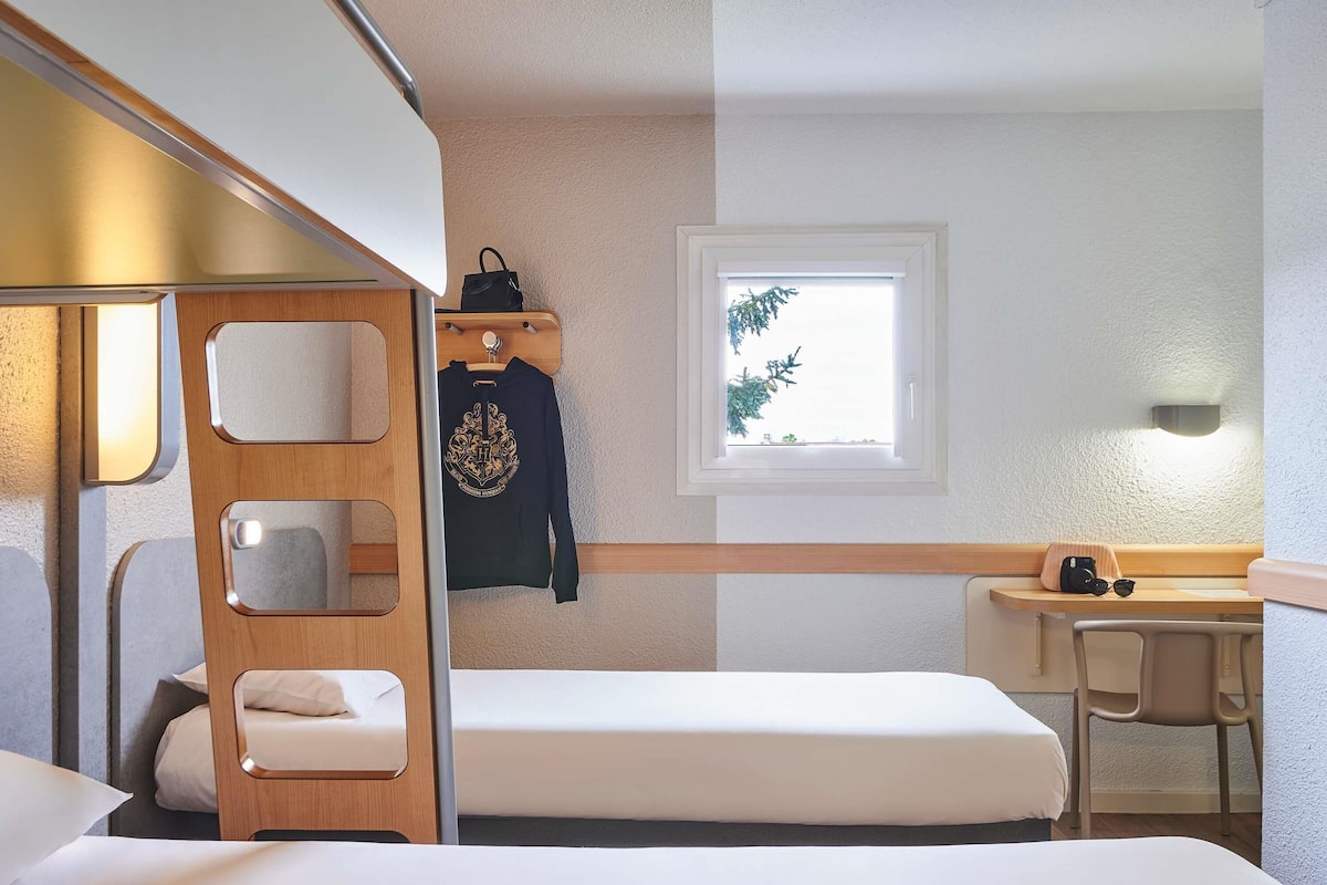 Habitación pequeña con literas, un escritorio, una silla, ventana con vistas y perchero con una chaqueta.
