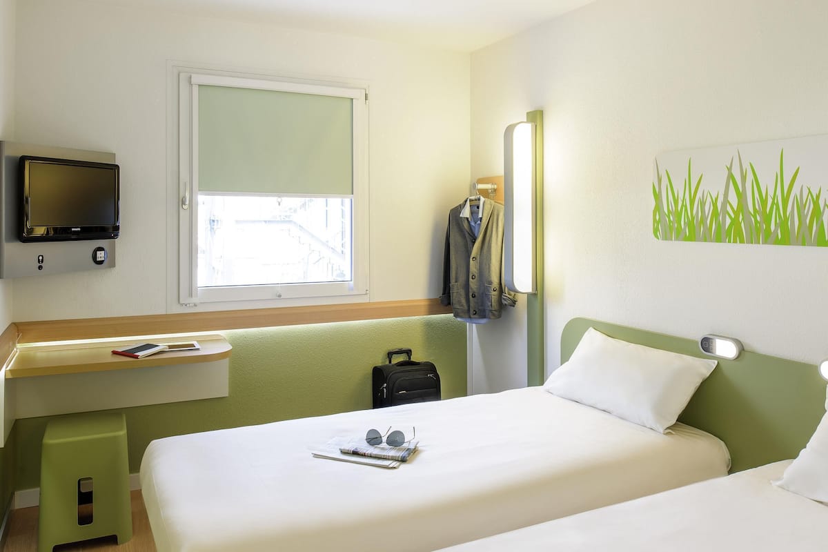 Una habitación de hotel con cama, mesita de noche, televisor, ventana y espejo fijado a la pared.