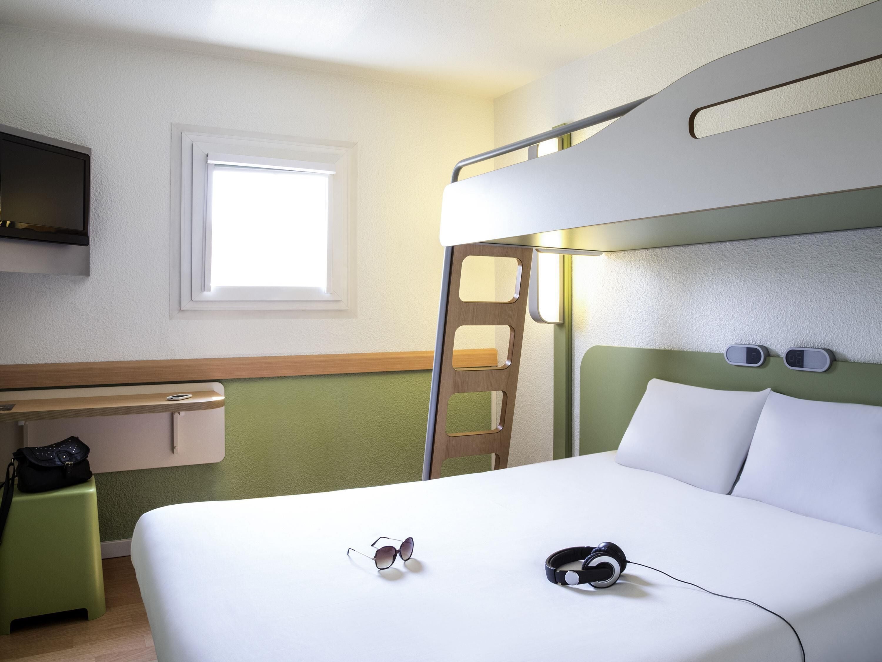 A bunk bed room with a desk, headphones, and sunglasses on the bed.