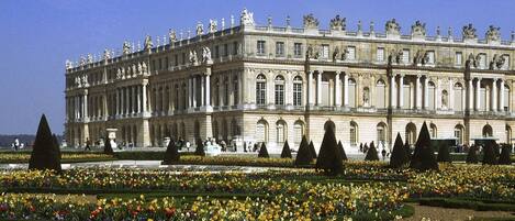 A large, historic building with symmetrical architecture and a formal garden in front.