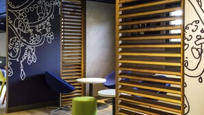 A modern interior with a wooden slatted partition, a green cushioned stool, and a small round table.
