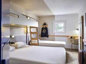 Habitación de hotel compacta con dos camas individuales, un escritorio pequeño, una ventana con vistas y una cama individual superior.