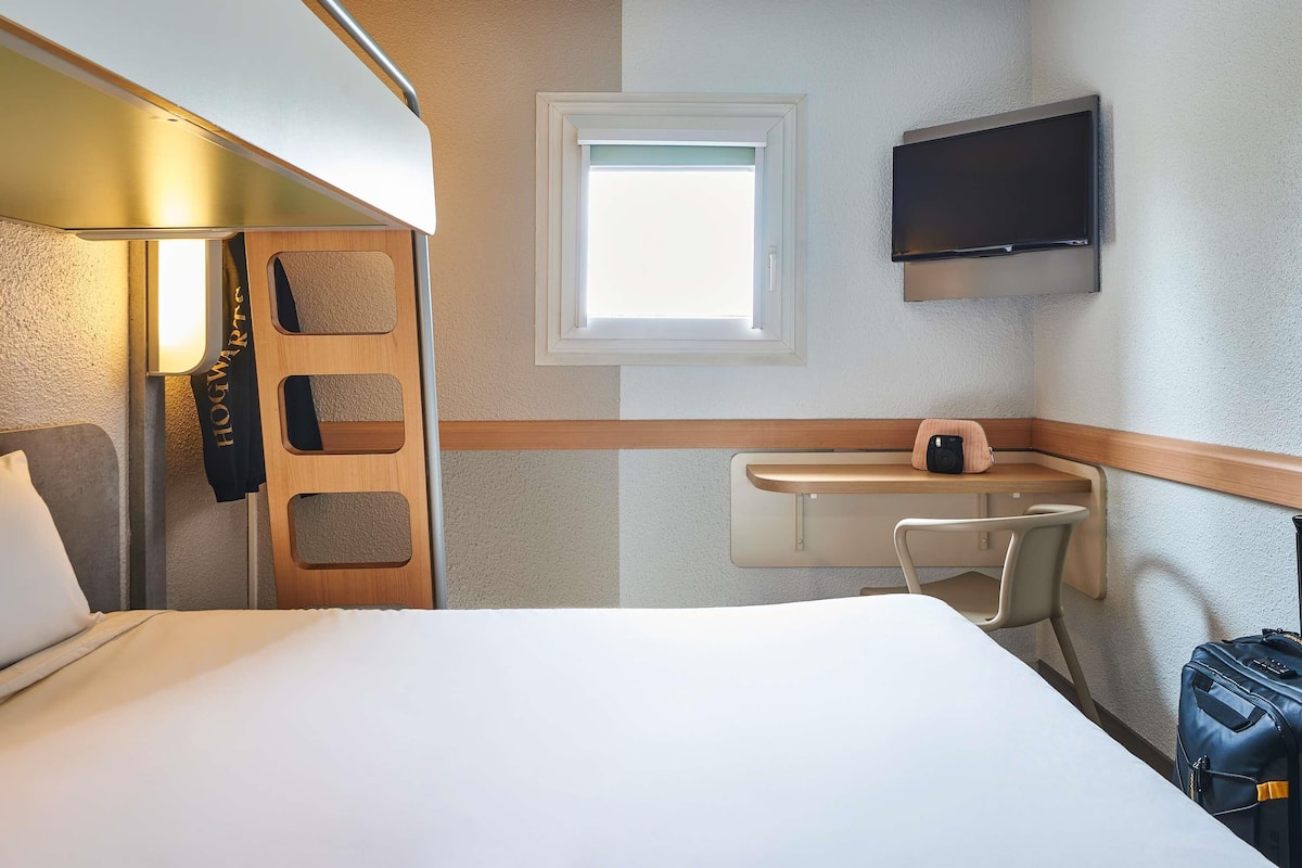 Una habitación de hotel con cama, escritorio, silla, televisor y maleta.