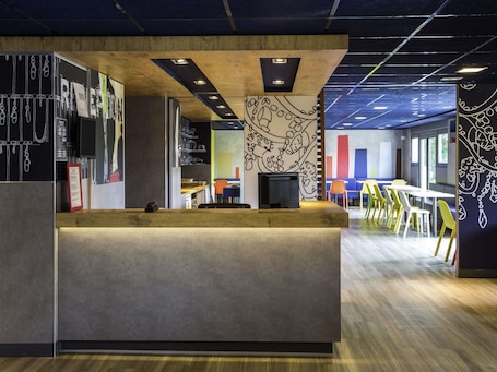 A modern office space with a reception desk, wooden ceiling, and colorful wall art.. ibis budget Versailles Chateau Saint Cyr