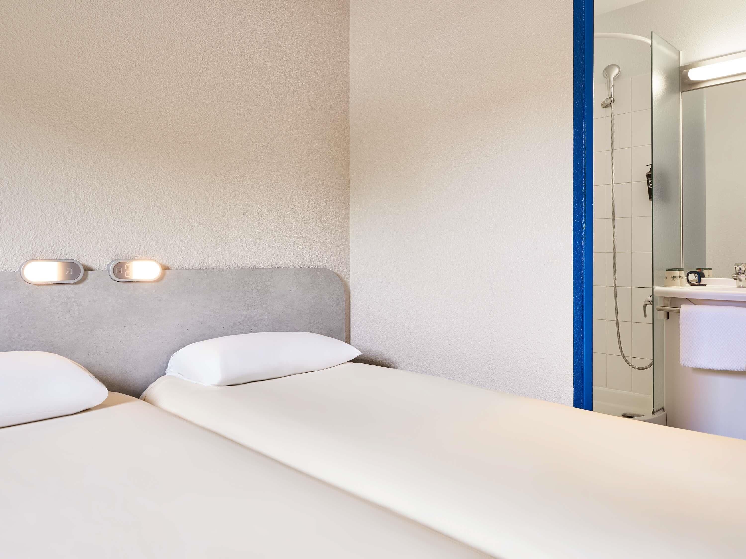A hotel room with two beds, a shower, and a mirror.