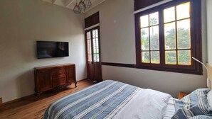 A bedroom with a bed, a wooden dresser, a television on the wall, and a window with a view of greenery. - Flying Dog Hostel B&B (Lima)