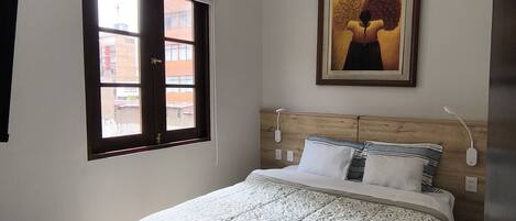 Quarto com cama, janela, pintura e cabeceira de madeira.