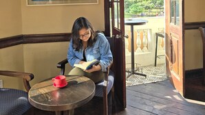A person reading a book at a table with a map on the wall and a wooden door leading outside. - Flying Dog Hostel B&B (Lima)