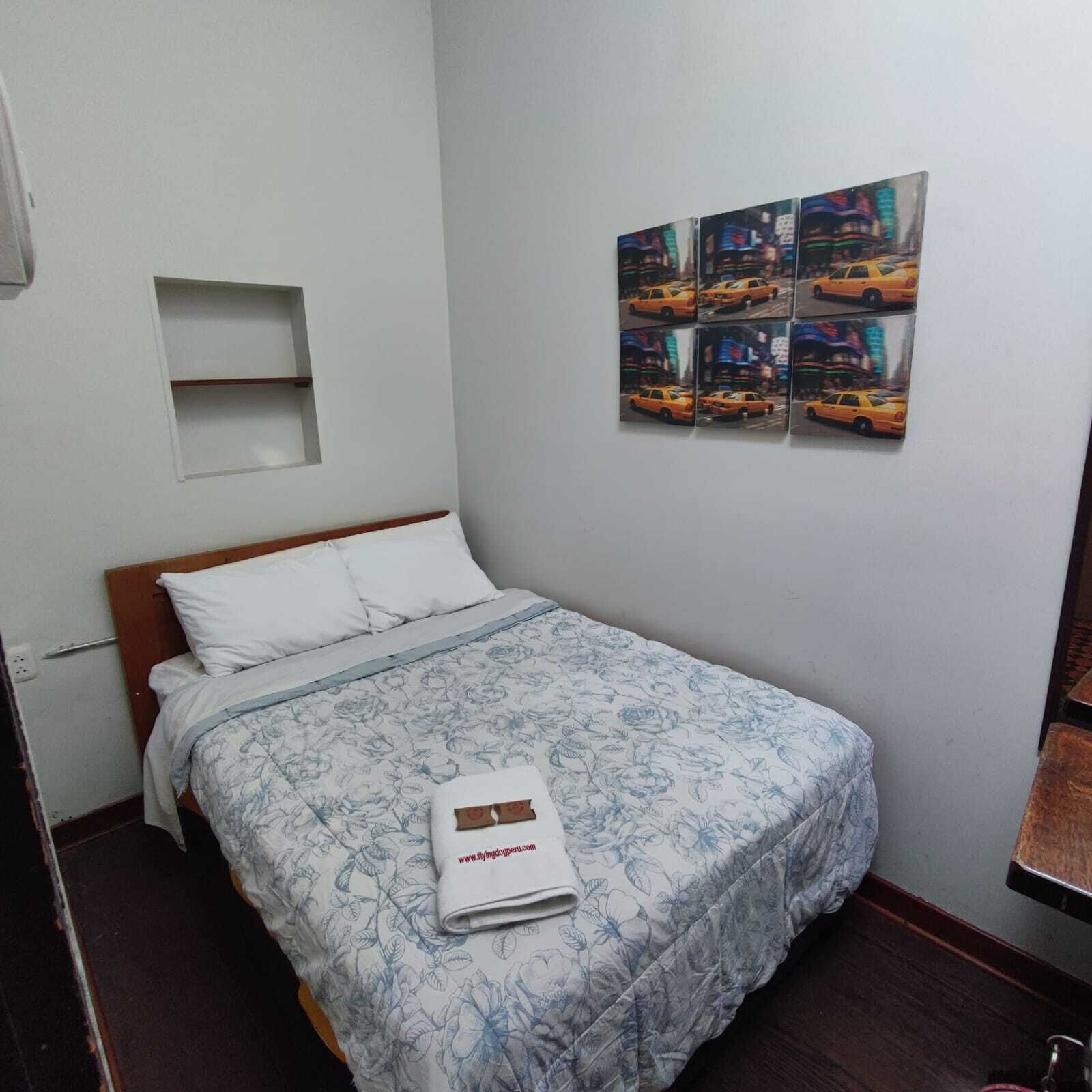 A small, neatly arranged bedroom with a single bed, a nightstand, and a wall-mounted shelf.
