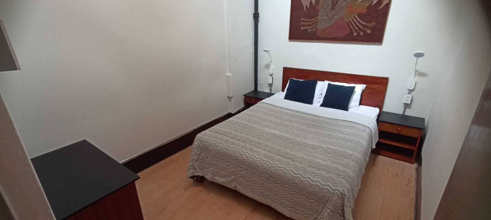 A small, neatly arranged bedroom with a bed, bedside tables, and a wall-mounted artwork.