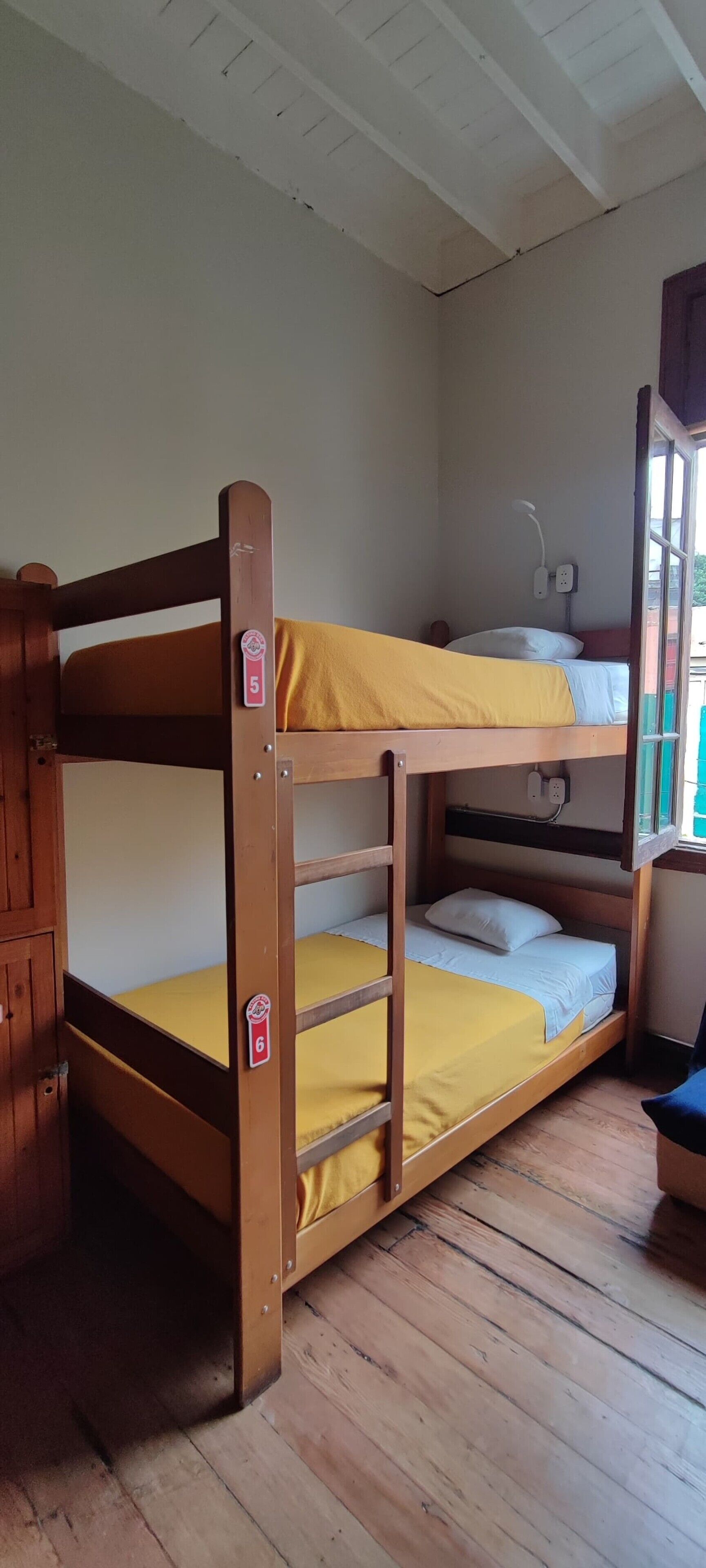 Una cama litera con colchón amarillo, cabecero de madera y enchufe de pared blanco.