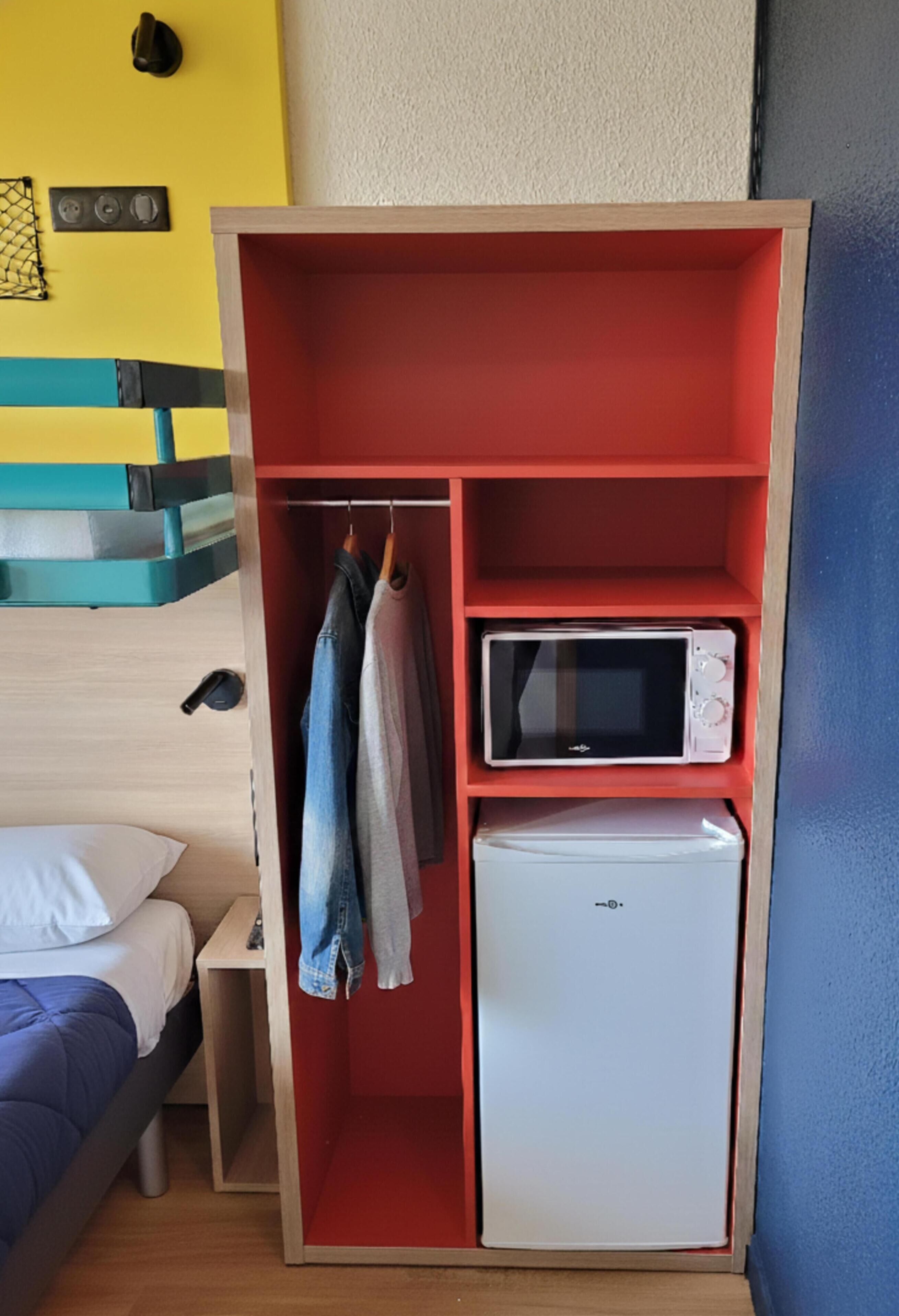 A compact room with a red wardrobe, a microwave, and a mini fridge.