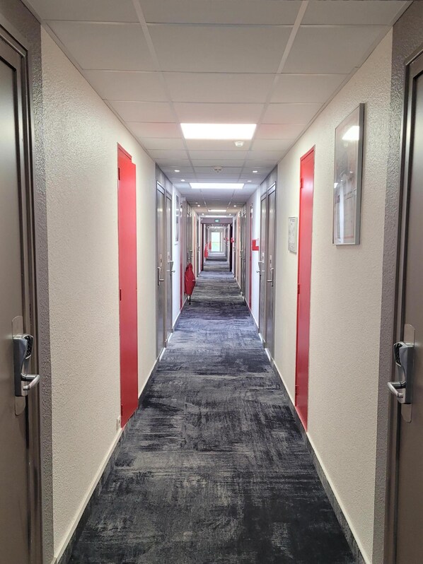 A hotel corridor with a carpeted floor, red doors, and a long hallway.