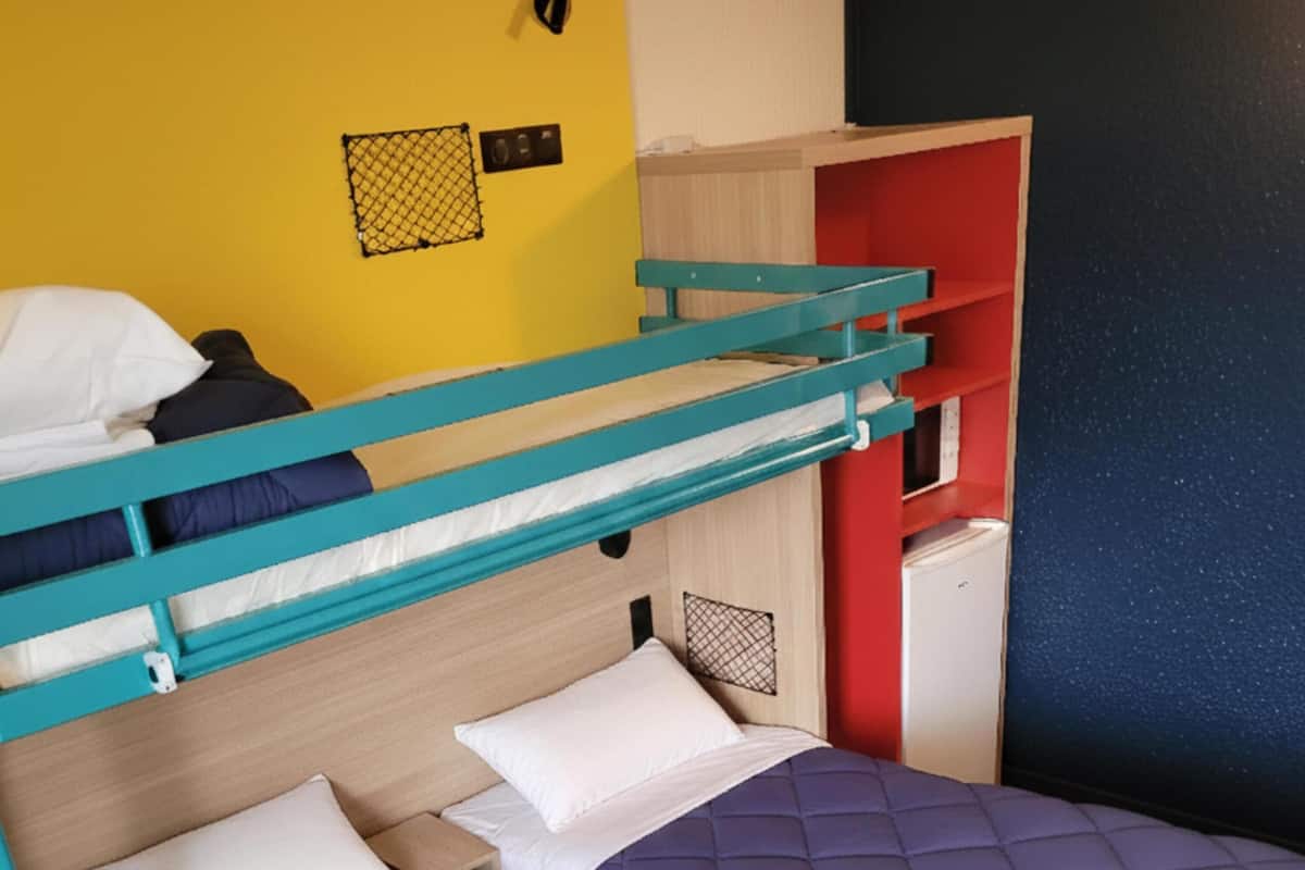 Una cama litera con cabecera de madera, un escritorio pequeño y un estante rojo.
