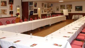 Une salle de conférence avec une longue table préparée pour une réunion, entourée de chaises rouges, et des murs ornés d’œuvres d’art encadrées.