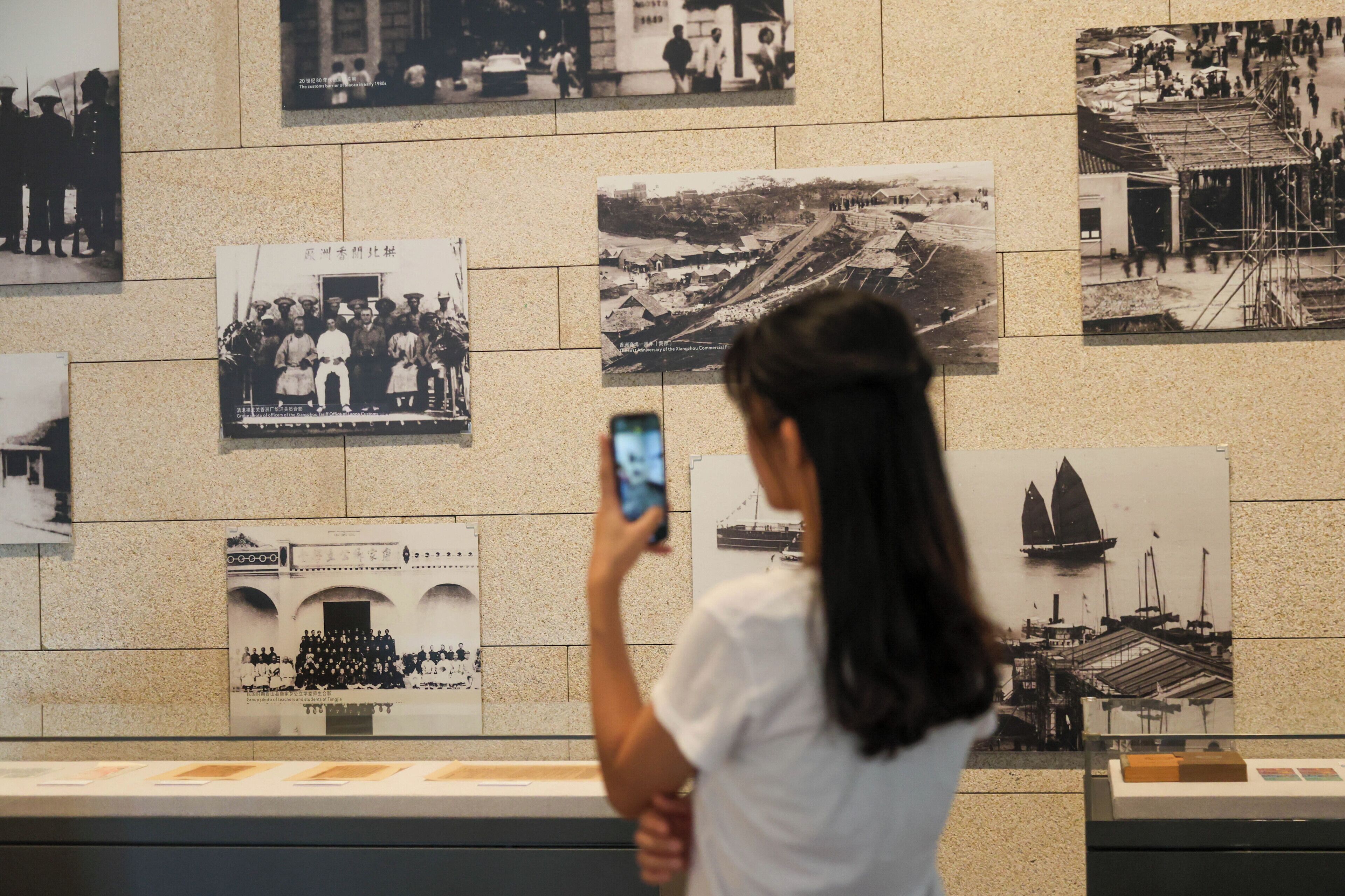 Una persona fotografiando una pared con fotografías históricas.