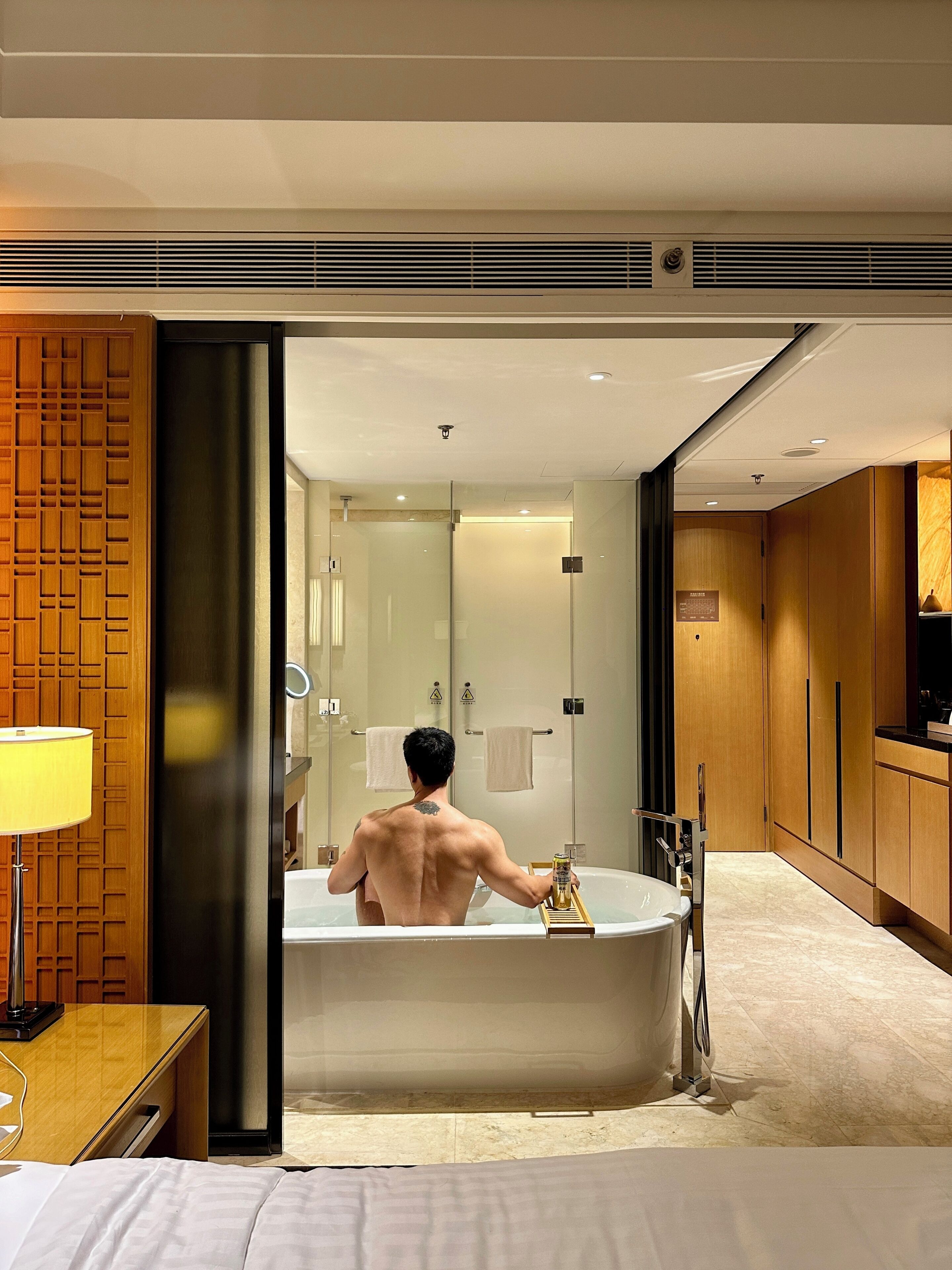 A modern hotel bathroom with a large bathtub, a wooden vanity, and a mirror.