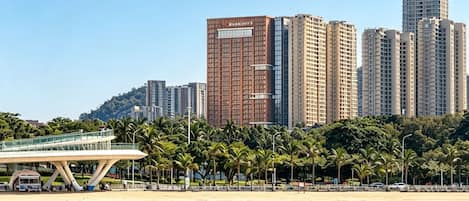 A coastal cityscape with high-rise buildings, a beach, and a pedestrian bridge.