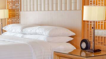 A neatly made bed with white linens, a glass side table with a lamp, and a wooden headboard with a decorative panel.