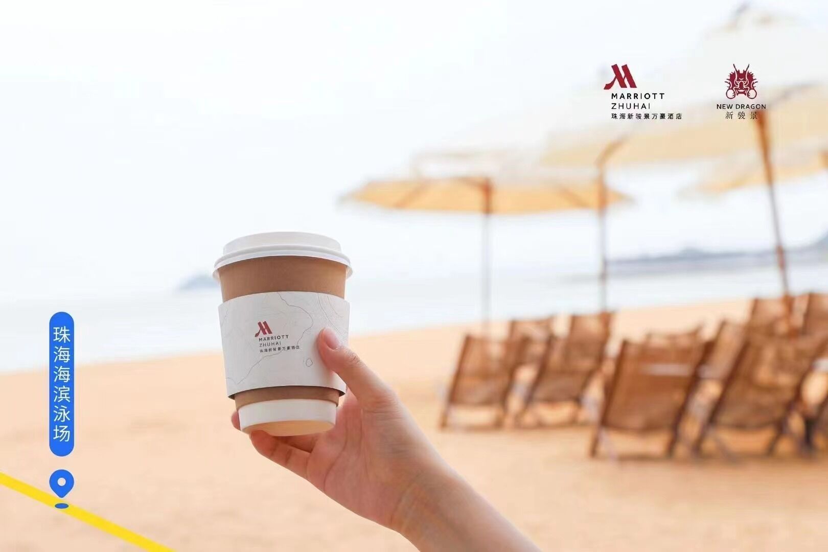 Una mano sostiene una taza de café con la marca Marriott ZHUHAI, con una playa y sombrillas al fondo.