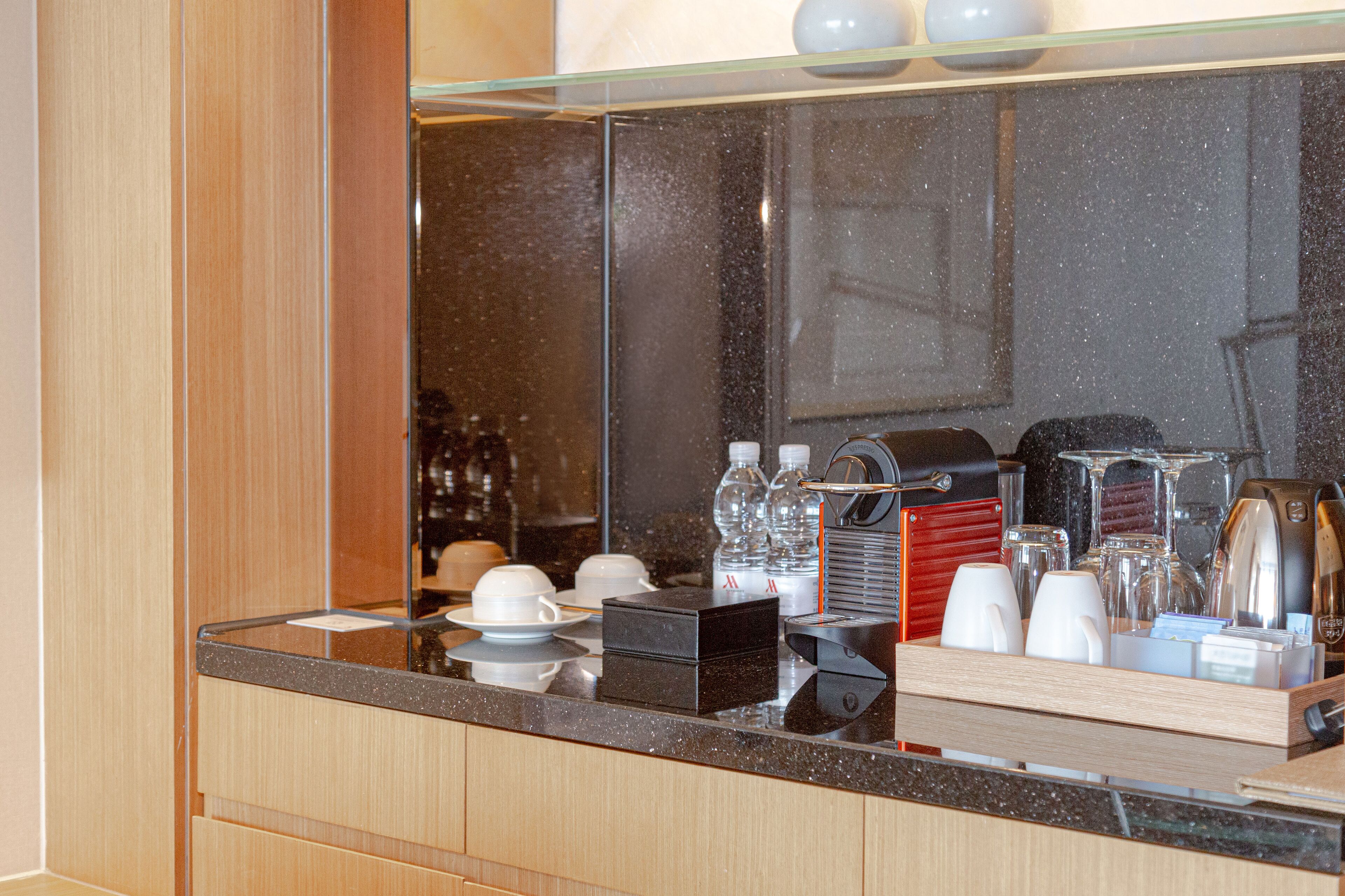 A hotel room's breakfast bar with a coffee machine, cups, and a glass display case.