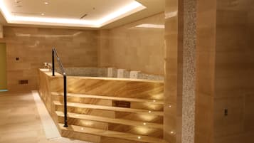 A modern hotel lobby with marble flooring, a central staircase, and a reception desk.