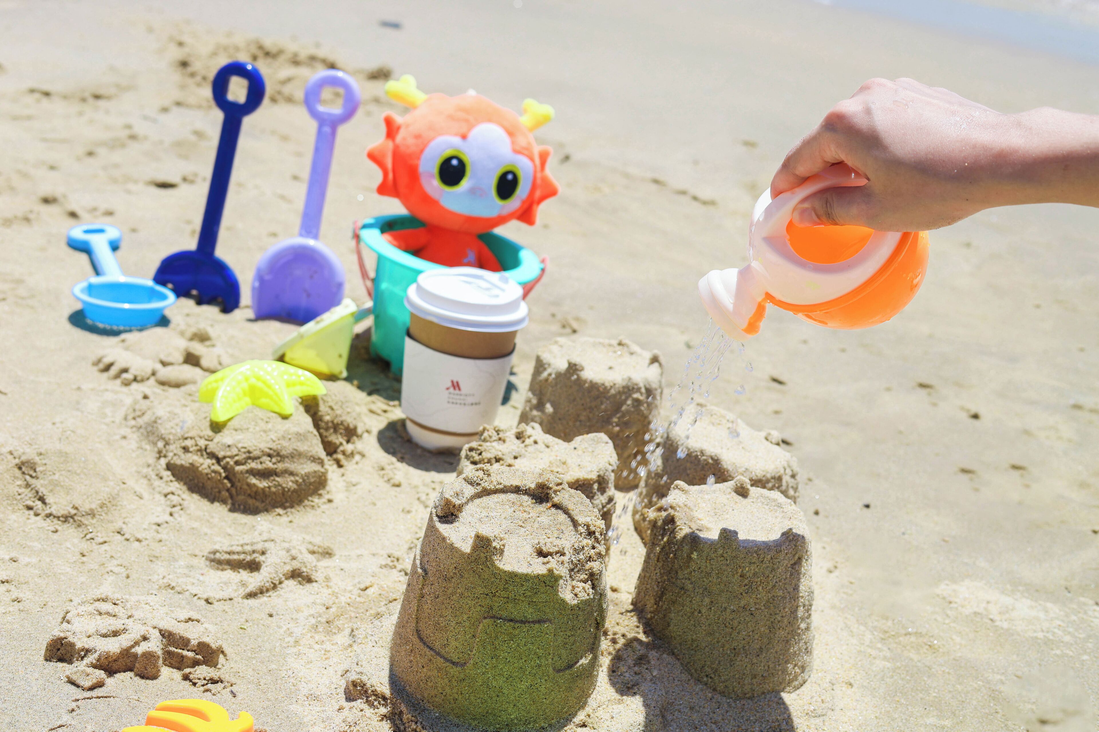 A sandy beach with a child's sandcastle, a toy car, and various beach toys.