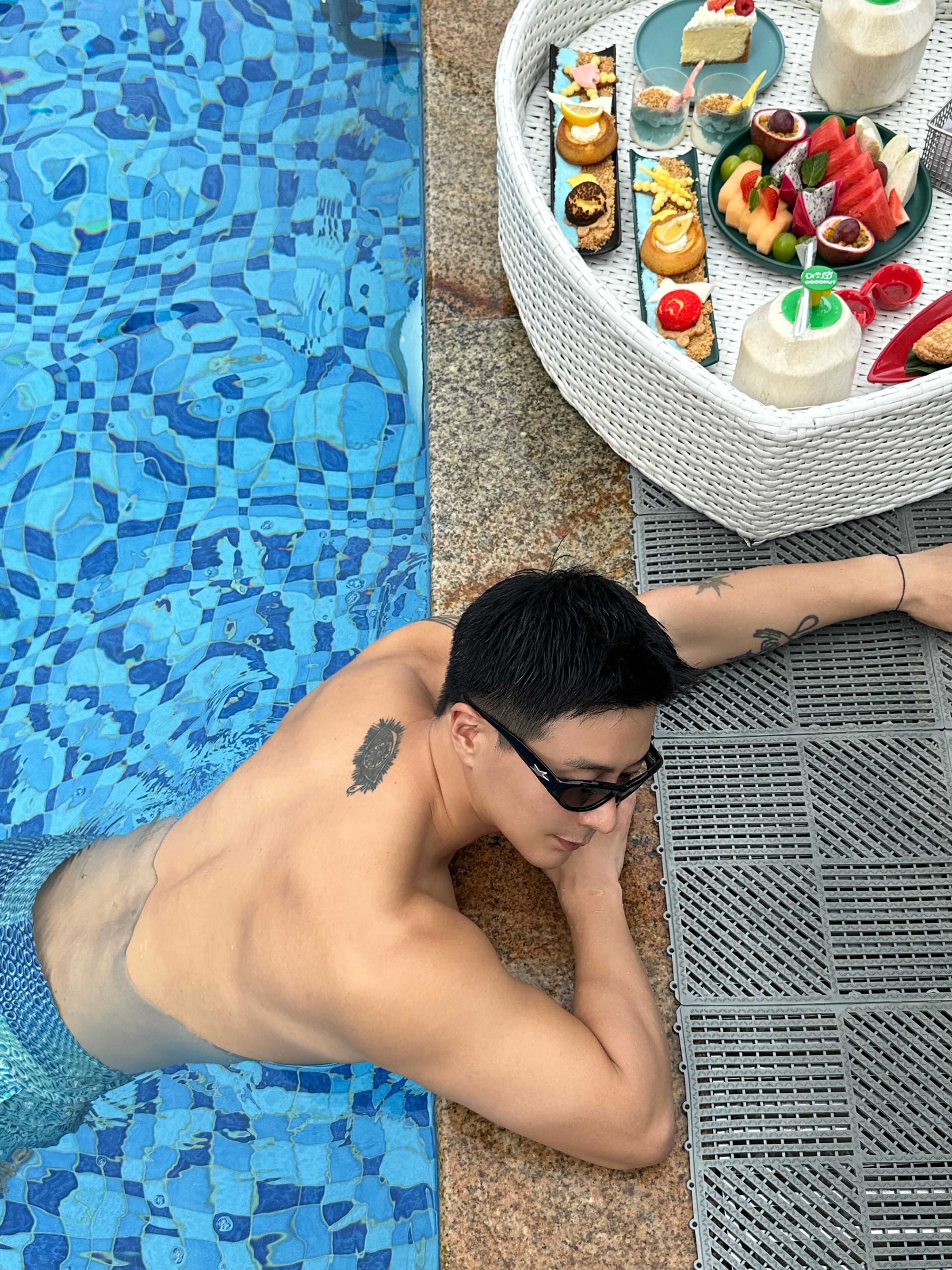 Una persona recostada junto a una piscina, con una cesta de mimbre que contiene comida y bebidas.