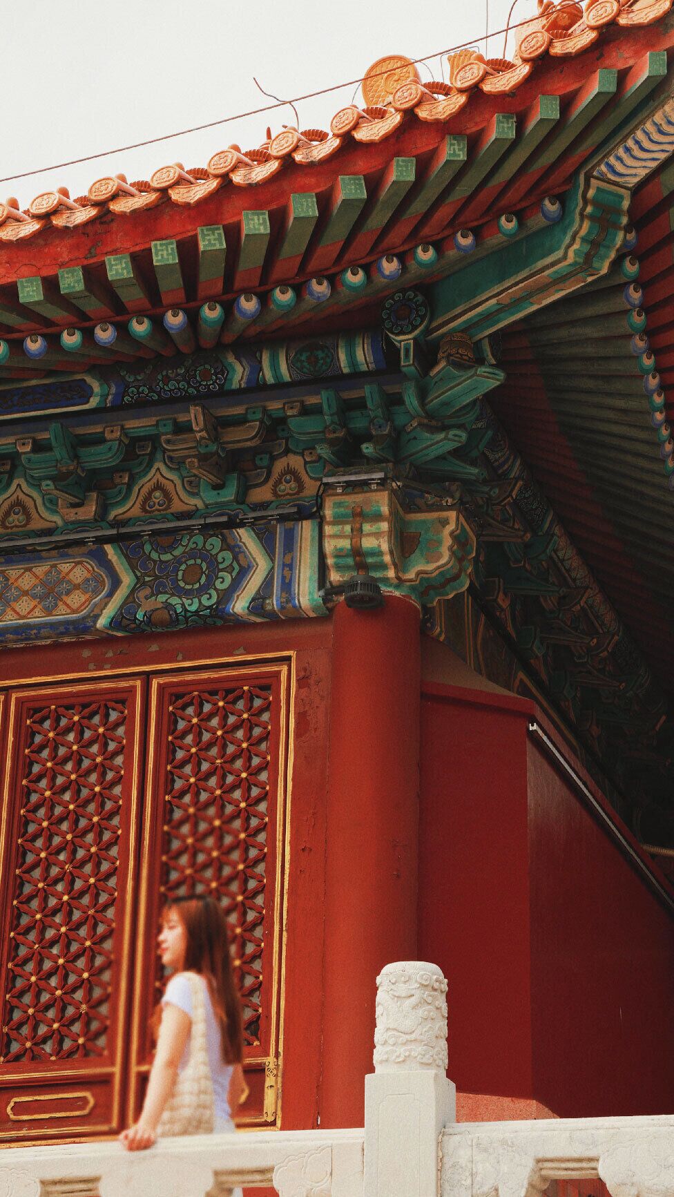 A traditional building with ornate roof tiles, a large decorative screen, and a person walking in front.