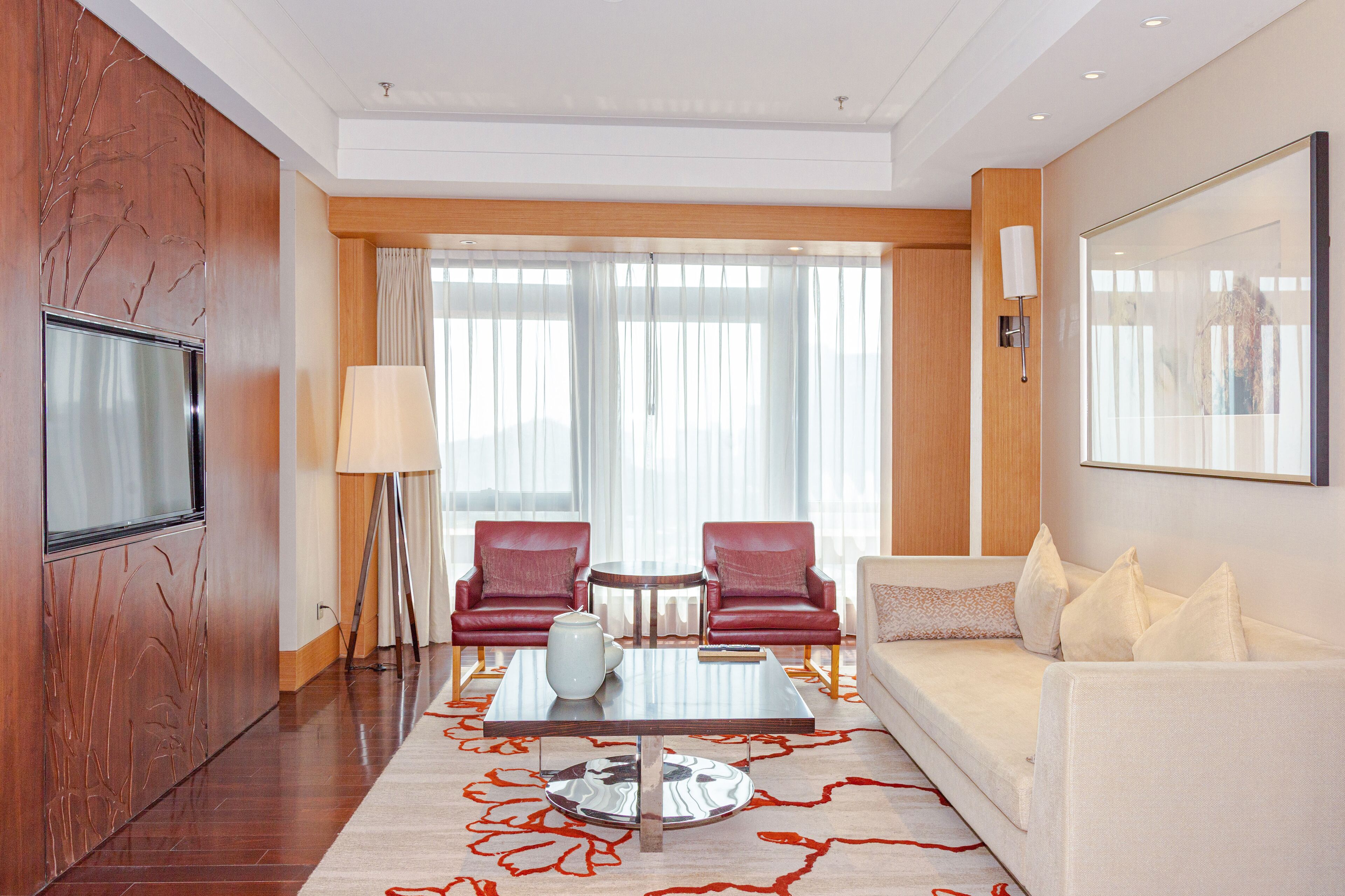 A hotel room with a flat-screen TV, two leather chairs, a sofa, a coffee table, and a large window with curtains.