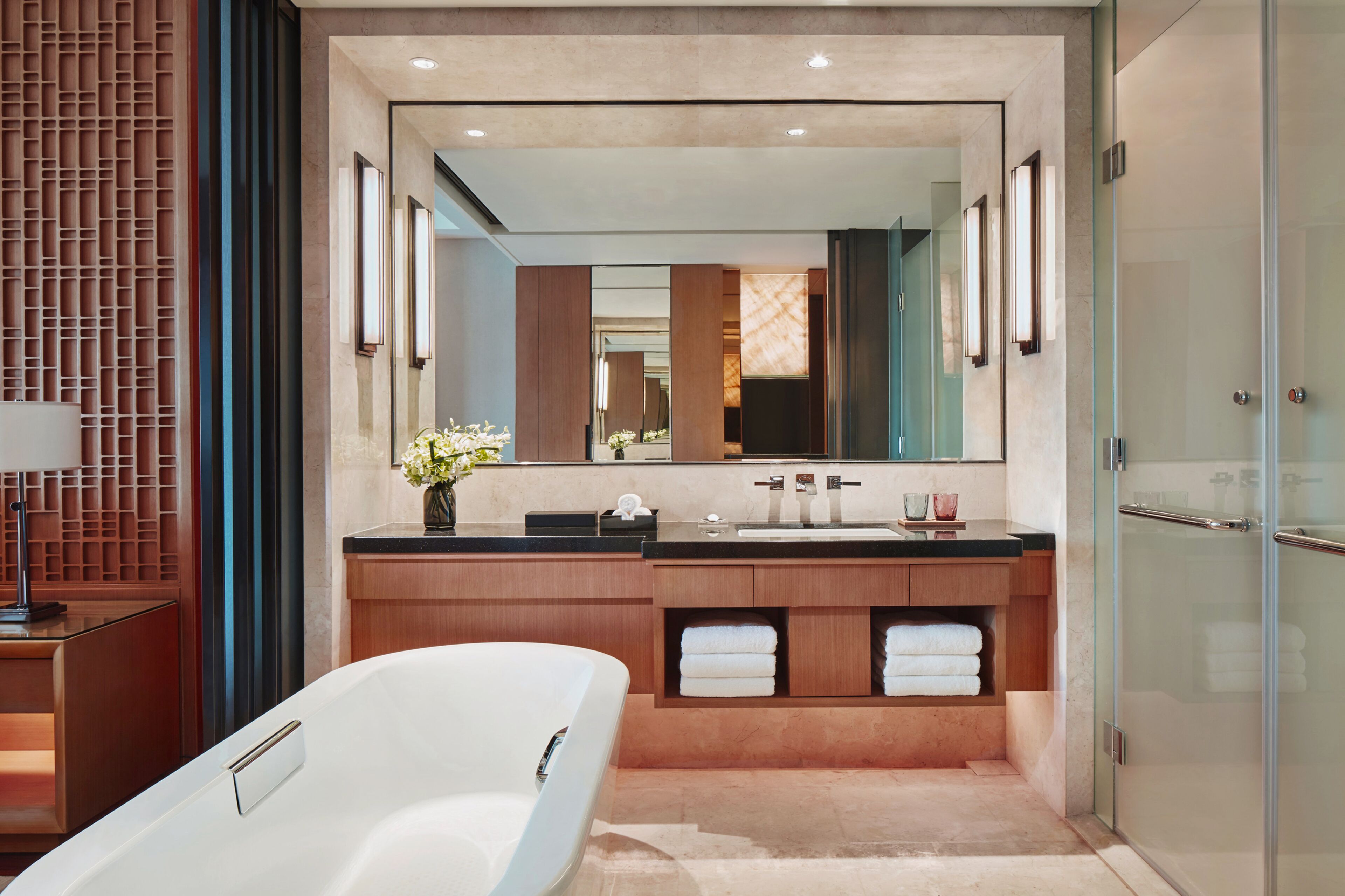 A modern bathroom with a large mirror, a bathtub, a vanity with a sink, and a glass shower enclosure.