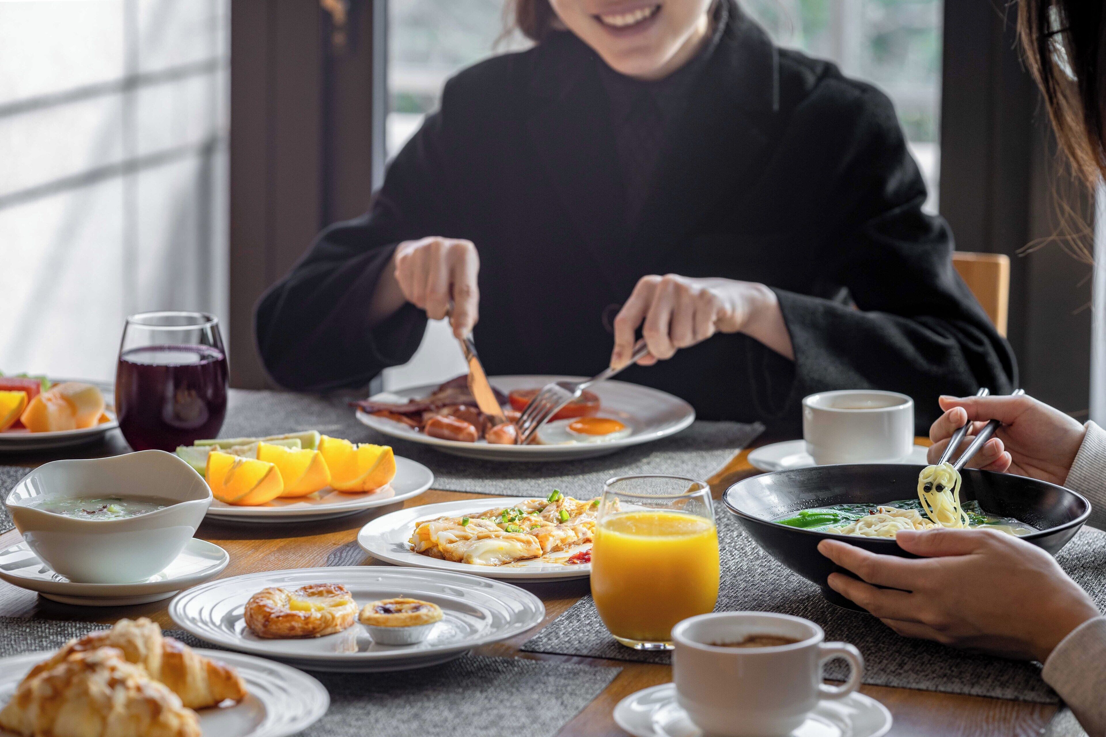 A breakfast setting with various dishes, a bowl of soup, and a glass of orange juice.