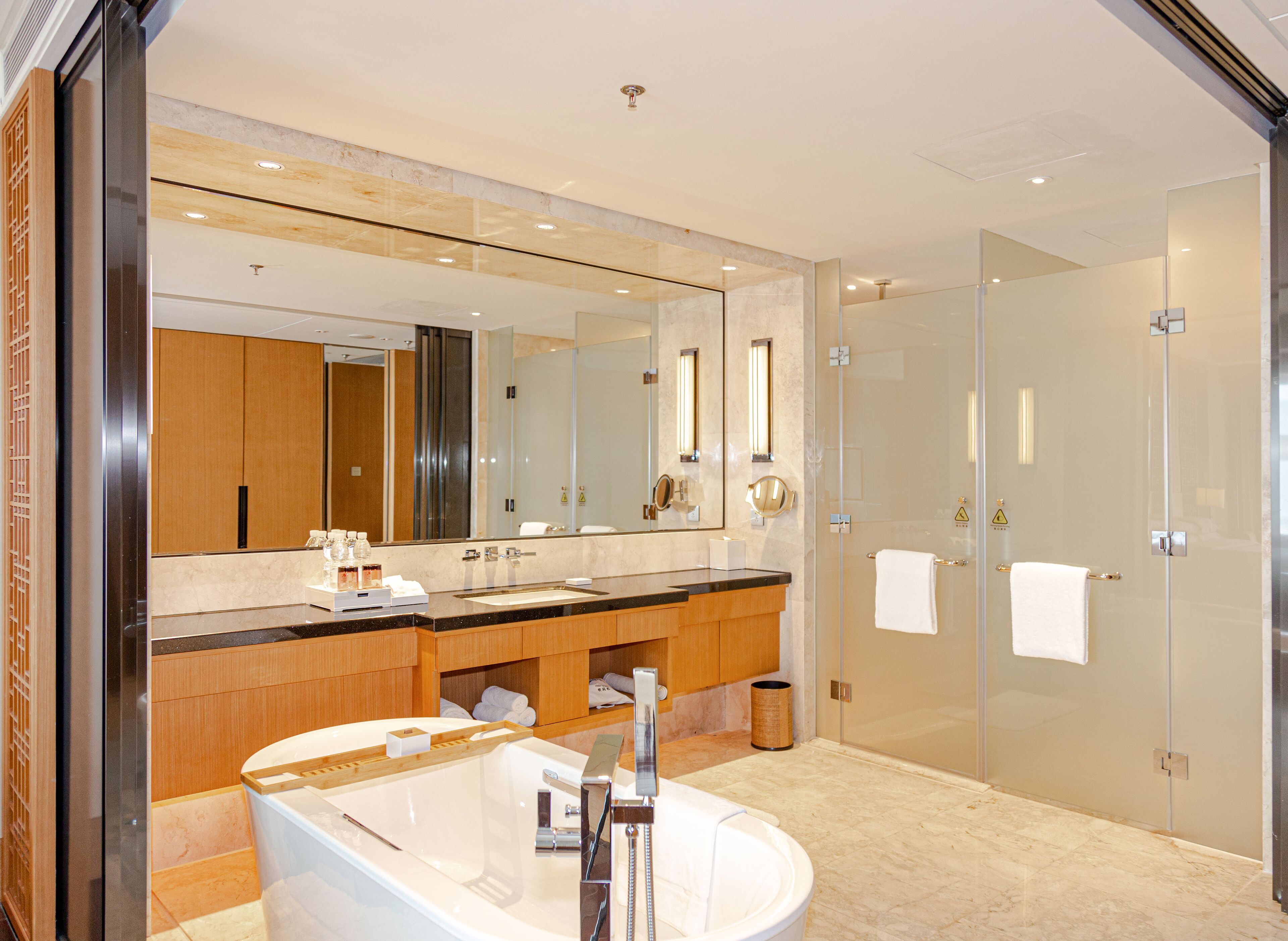 A modern bathroom with a large mirror, a bathtub, a sink, and a glass-enclosed shower.