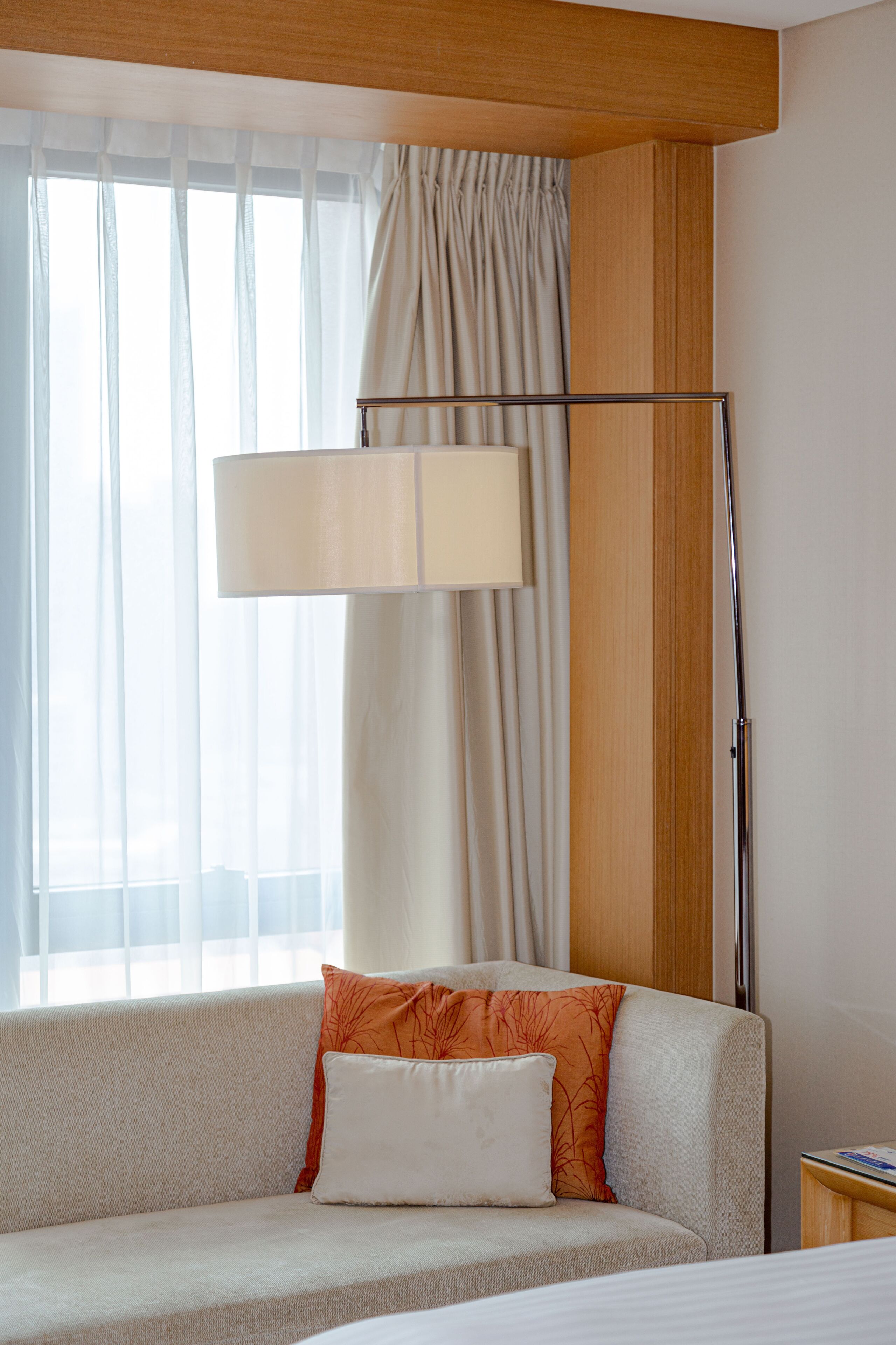 Una habitación de hotel con sofá, lámpara y ventana con cortinas.