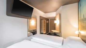 Ein Hotelzimmer mit einem Bett, einem an der Wand befestigten Fernseher, einem Spiegel und einem Stadtbild.