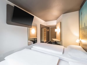Une chambre d’hôtel avec un lit, un téléviseur fixé au mur, un miroir et un tableau représentant un paysage urbain.