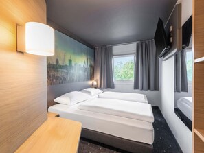 Habitación de hotel con cama, escritorio, cuadro, ventana con cortinas y televisor de pantalla plana.
