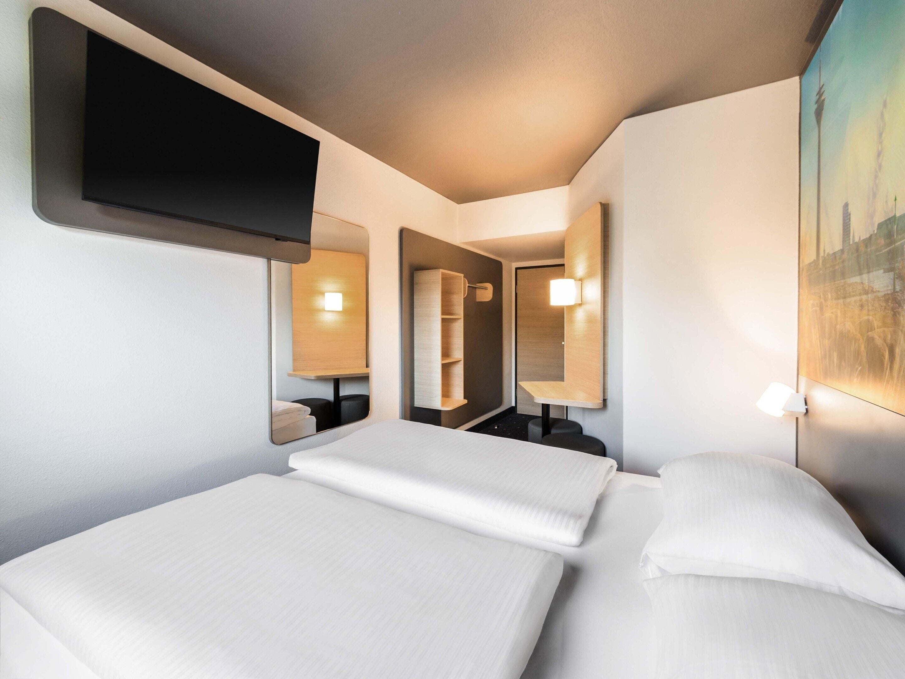 A hotel room with two beds, a flat-screen TV mounted on the wall, and a painting of a cityscape.