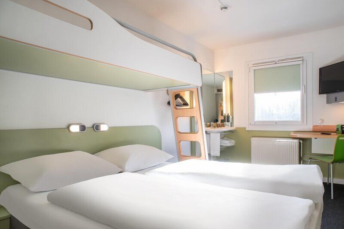 Une chambre d’hôtel avec deux lits, un bureau, une chaise, un miroir et une télévision.