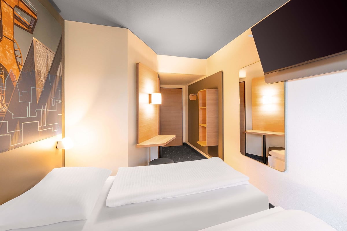 A hotel room with two beds, a hallway, and a bathroom.