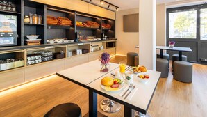 A modern breakfast setup with a buffet, seating area, and large windows. -  B&B HOTEL Essen-Nord (Essen)