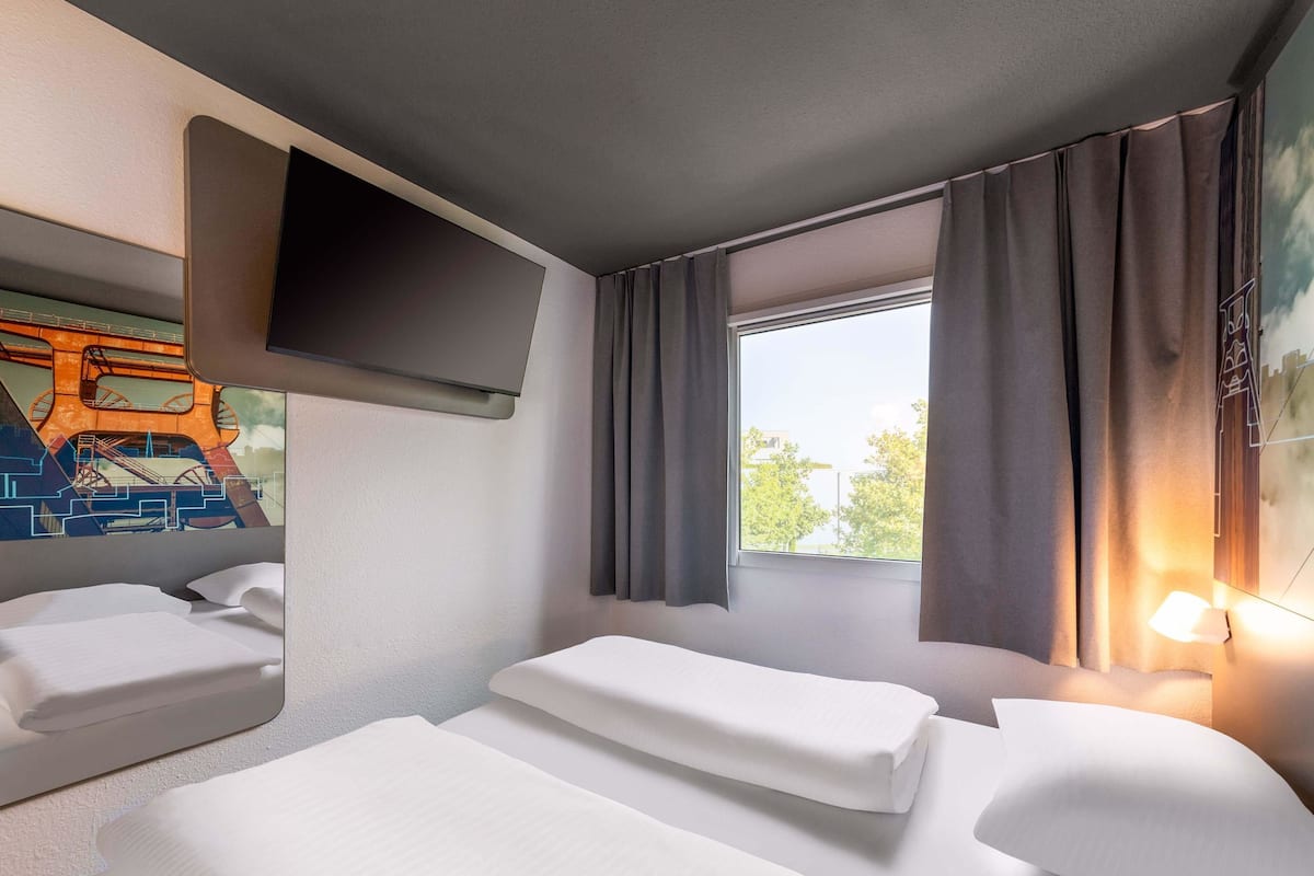 A hotel room with two beds, a flat-screen TV mounted on the wall, and a window with curtains.