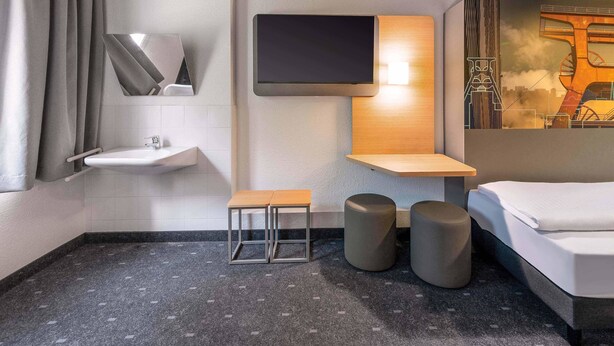 Un baño de hotel moderno con lavamanos, espejo, inodoro y cama.