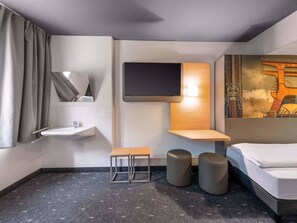 A modern hotel bathroom with a sink, mirror, toilet, and a bed. -  B&B HOTEL Essen-Nord (Essen)