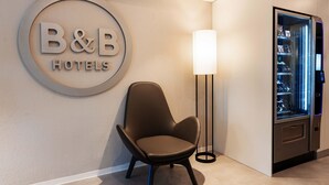 Zona de recepción de un hotel B&B con una silla moderna, un cartel en la pared y una máquina expendedora.
